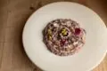 Risotto alla radicchio su piatto bianco, con noci e fiori edibili